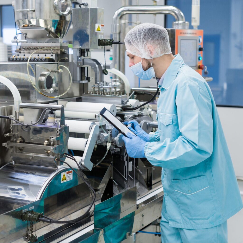 Pharmaceutical technician in cleanroom monitoring SAP-integrated manufacturing equipment with tablet