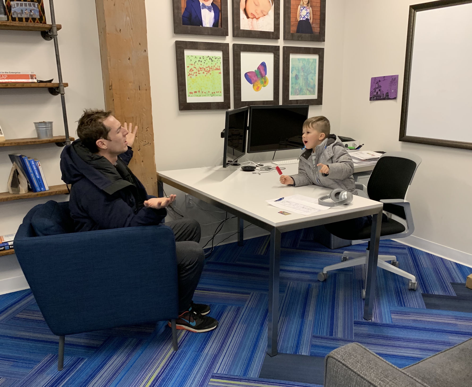 Gavin Quinn in his old office, sitting in the guest chair while his young son Andrew sits at the CEO desk holding a popsicle